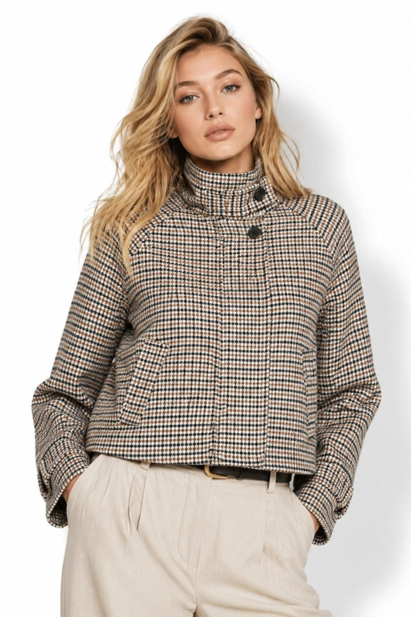 Front view of a blonde female model wearing a cropped brown and black houndstooth jacket with a high collar and neutral tailored trousers.