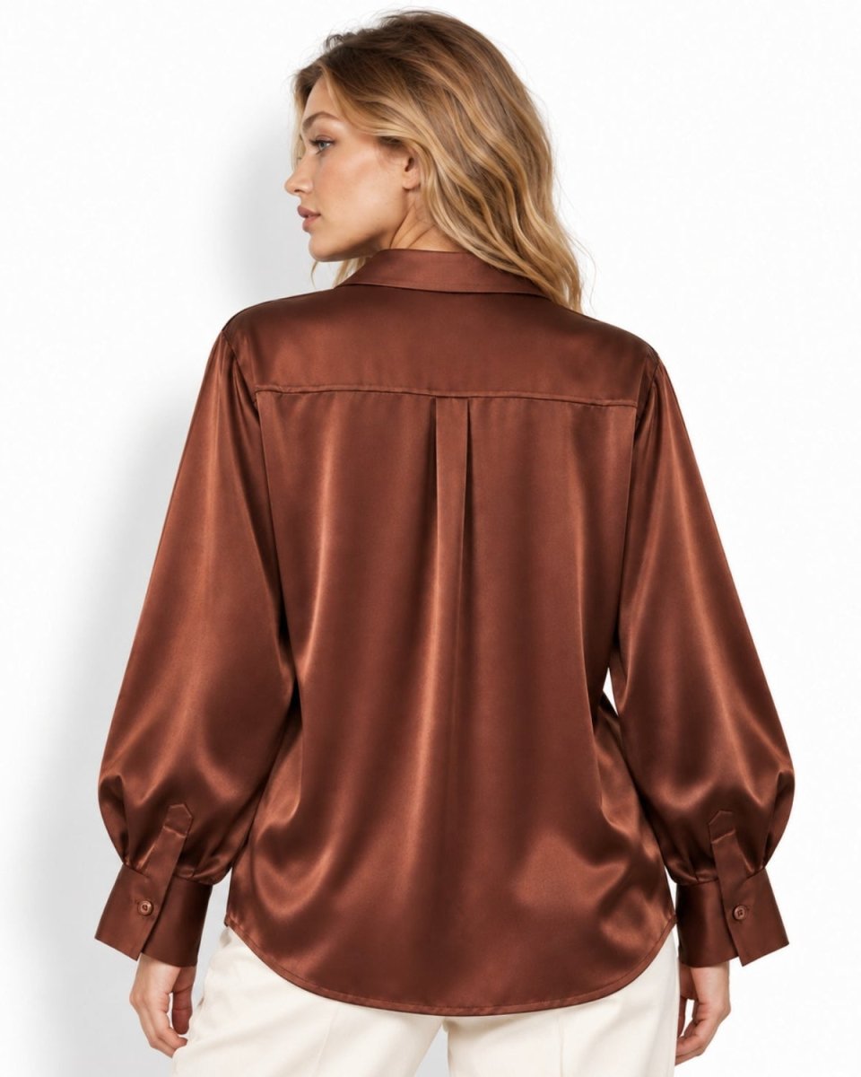 A woman shown from the back wearing a brown silk long-sleeve blouse with button cuffs, paired with off-white pants, against a plain white studio background.