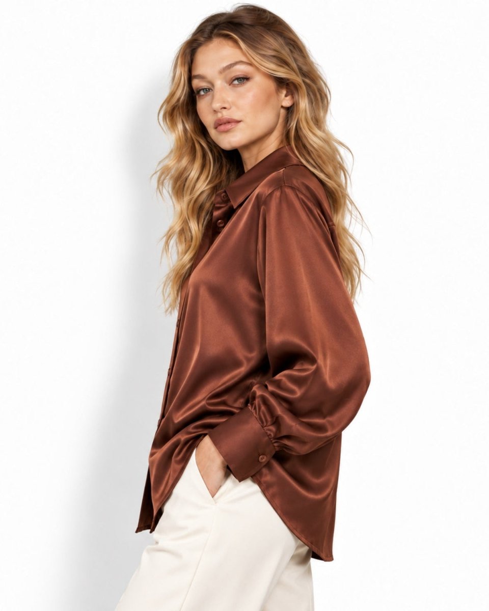 A woman wearing a brown silk button-up shirt and white pants, photographed against a clean white studio background.