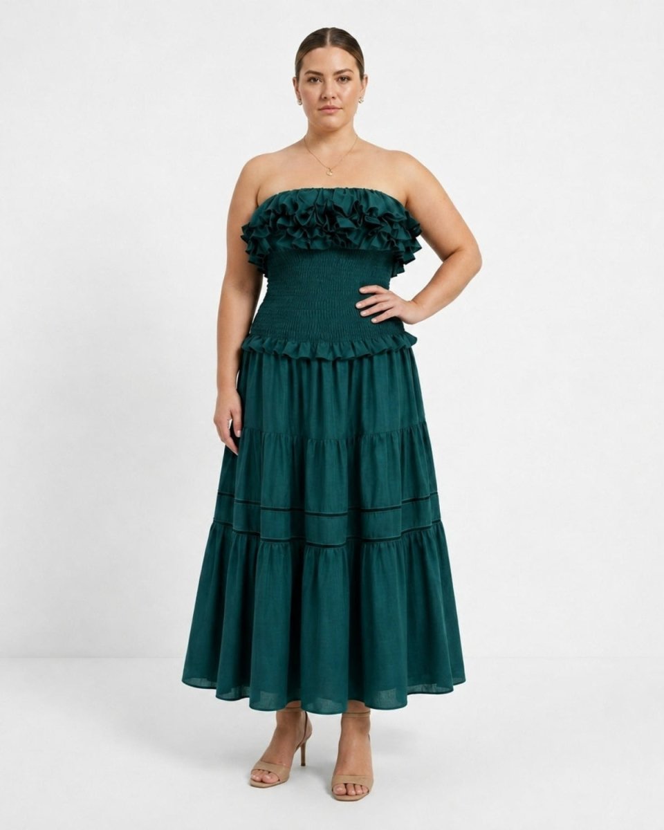 A woman modeling a strapless dark green tiered maxi dress with a ruffled sweetheart neckline, standing against a plain white studio background.