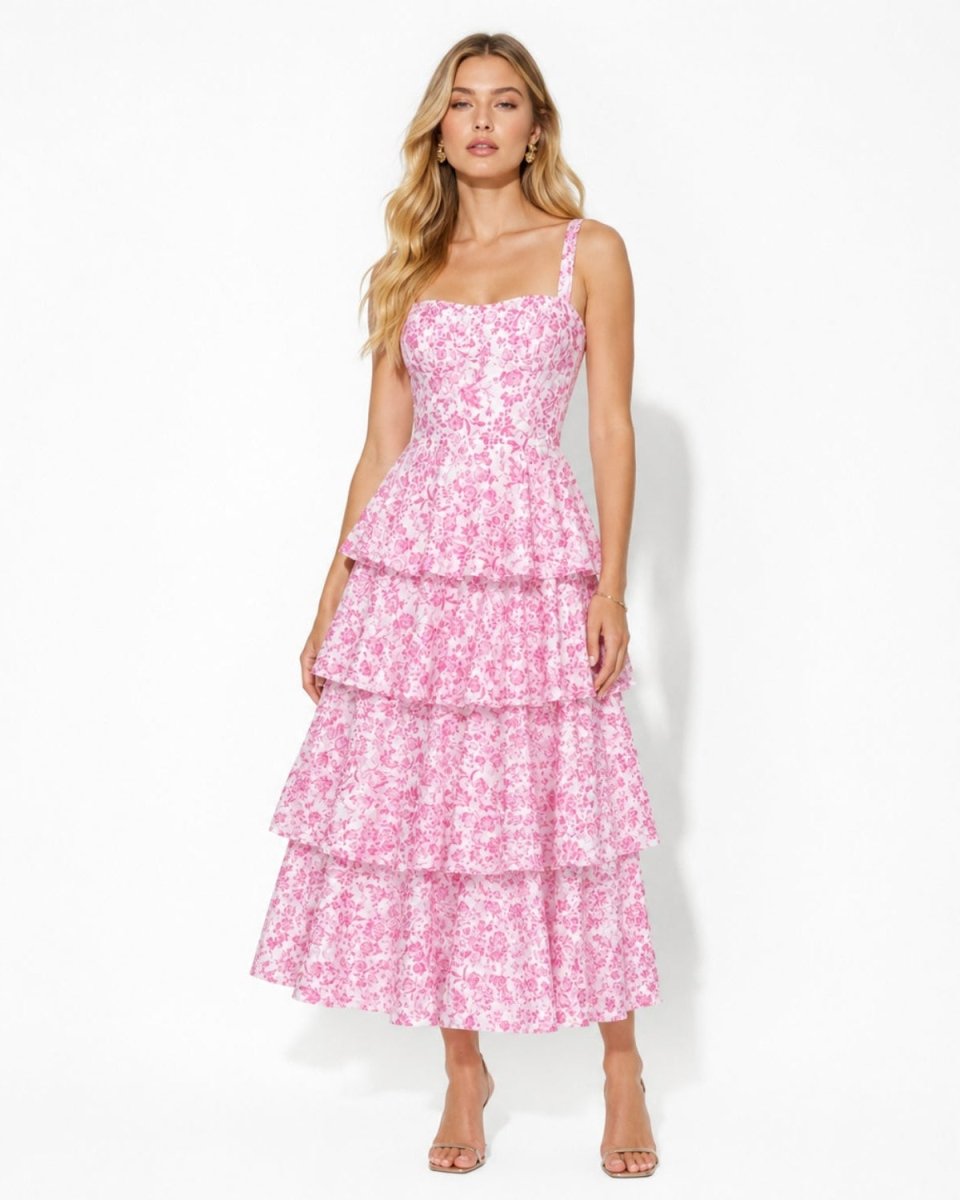 A woman modeling a pink floral tiered maxi dress with thin straps and a sweetheart neckline, standing against a plain white studio background.