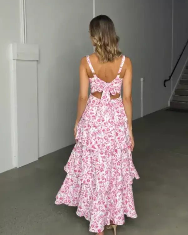 Model wearing the Denise pink floral tiered midi dress with a square neckline and open-back bow detail at a garden party