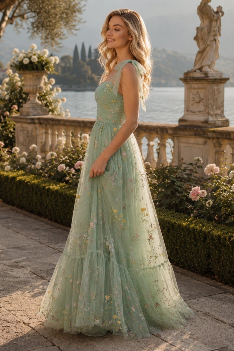 A woman wearing a sleeveless mint green tulle wedding dress with floral embroidery, standing outdoors in front of a stone balustrade and lake.