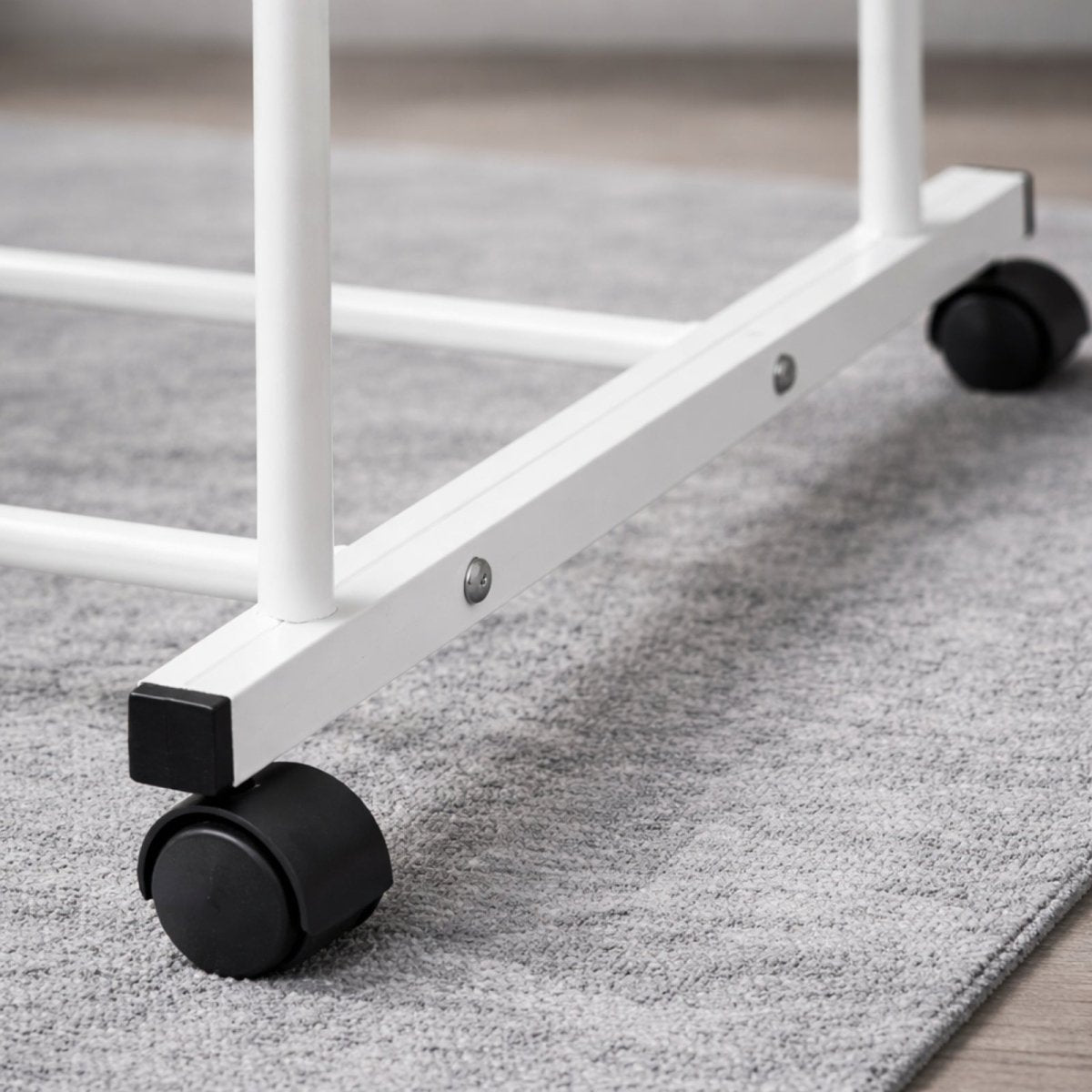 Close-up detail of a smooth-gliding, lockable black caster wheel on the base of the white Kouvr garment rack, positioned on a grey area rug.
