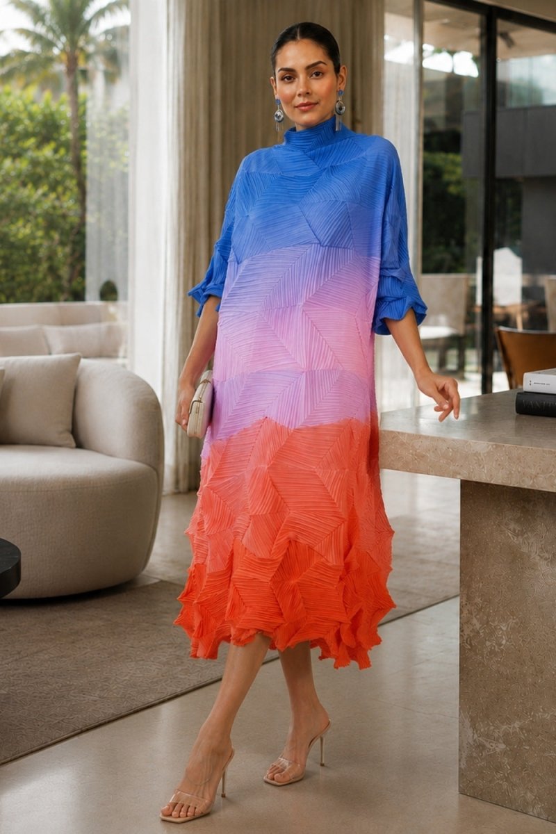 A woman models a high-neck, tiered midi dress with a vibrant blue, purple, and orange ombre gradient. The dress features a structured pleated upper bodice and a flowing, ruffled lower skirt.