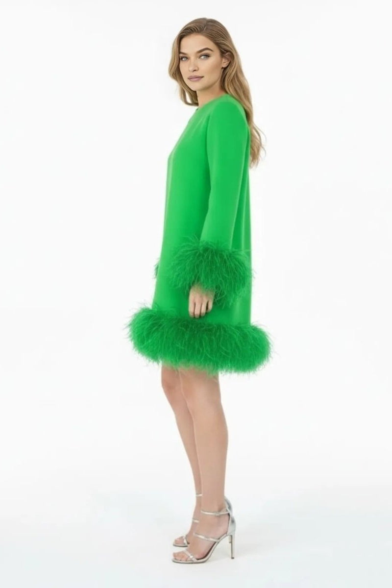 Side profile of a model in the Kouvr green A-line mini dress, highlighting the silhouette and plush feather details on the sleeve and hem.