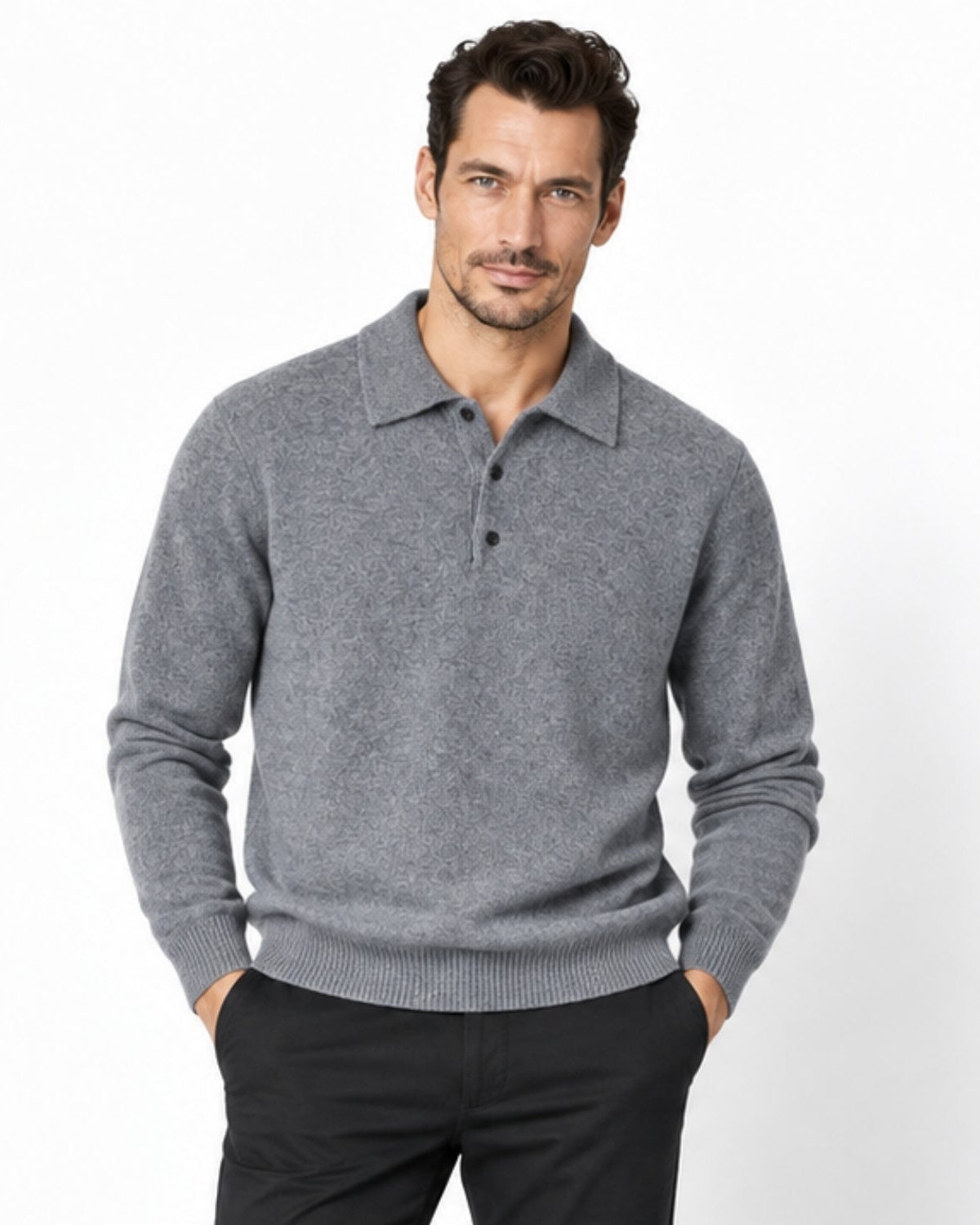 A man wearing a gray knit polo sweater and black trousers, standing against a plain white studio background.