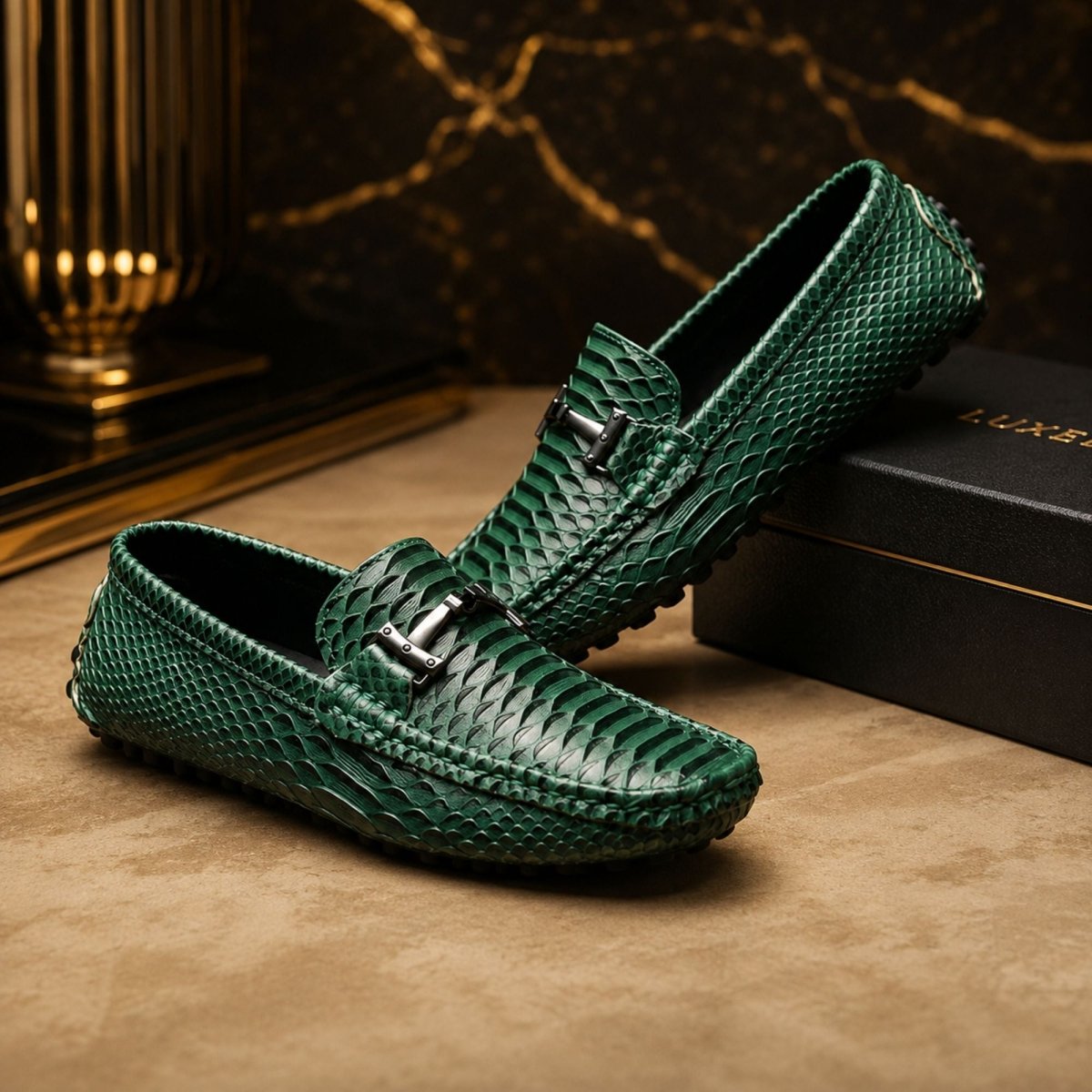 A pair of dark green snakeskin-patterned loafers with silver-tone buckle details, displayed on a brown textured surface next to a black box with gold lettering.