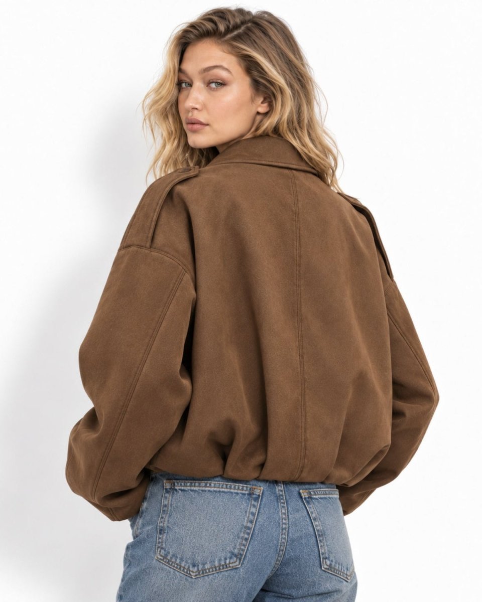 A woman wearing an oversized brown suede jacket and light blue jeans, photographed from the back against a clean white studio background.