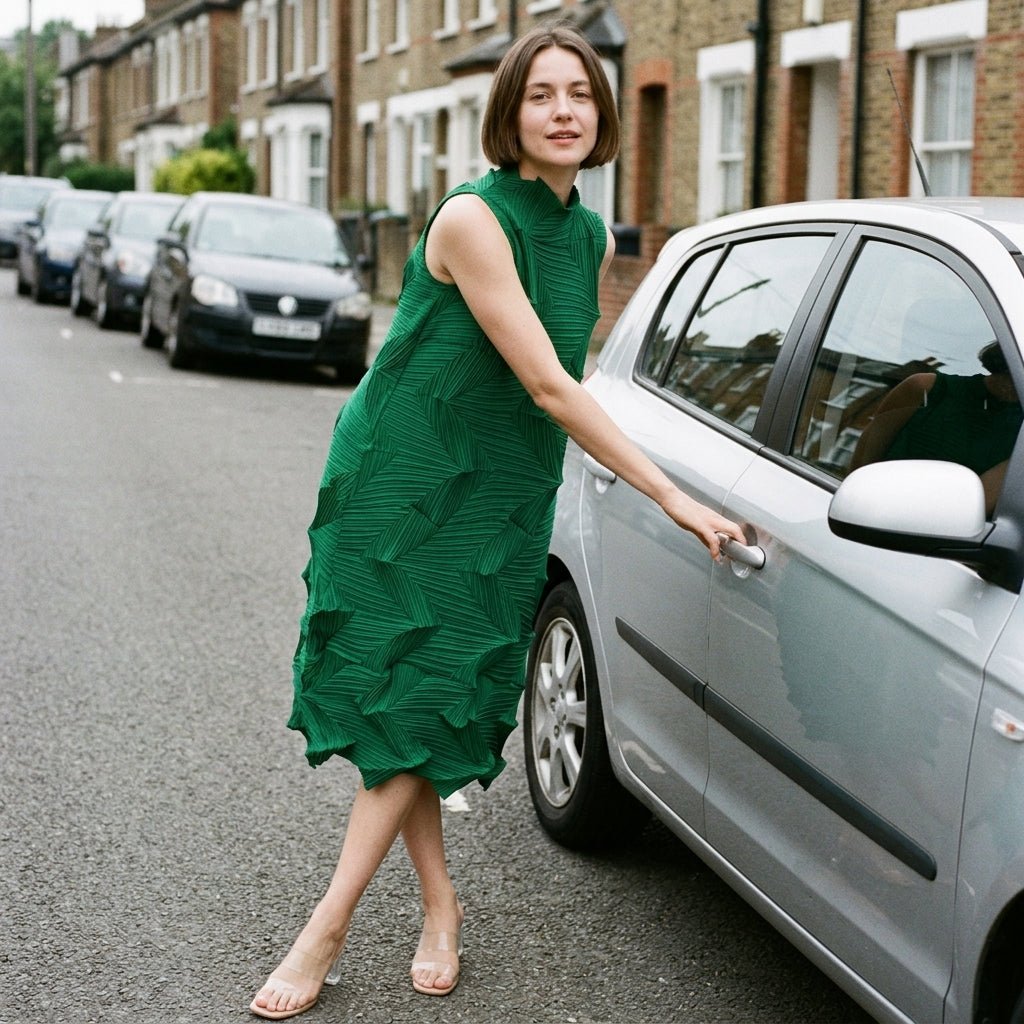 Sophisticated woman in an emerald green pleated midi dress opening a silver car door on a residential city street.