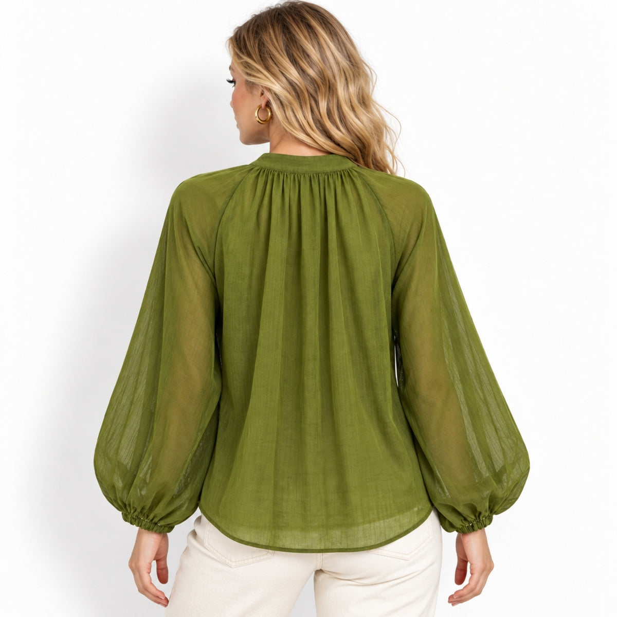 A woman viewed from the back wearing a sheer olive green long-sleeve blouse with a gathered neckline and balloon sleeves, paired with light cream pants, against a plain white background.