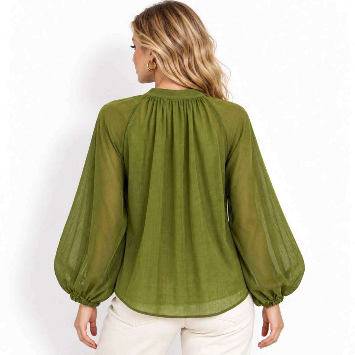 A woman viewed from the back wearing a sheer olive green long-sleeve blouse with a gathered neckline and balloon sleeves, paired with light cream pants, against a plain white background.