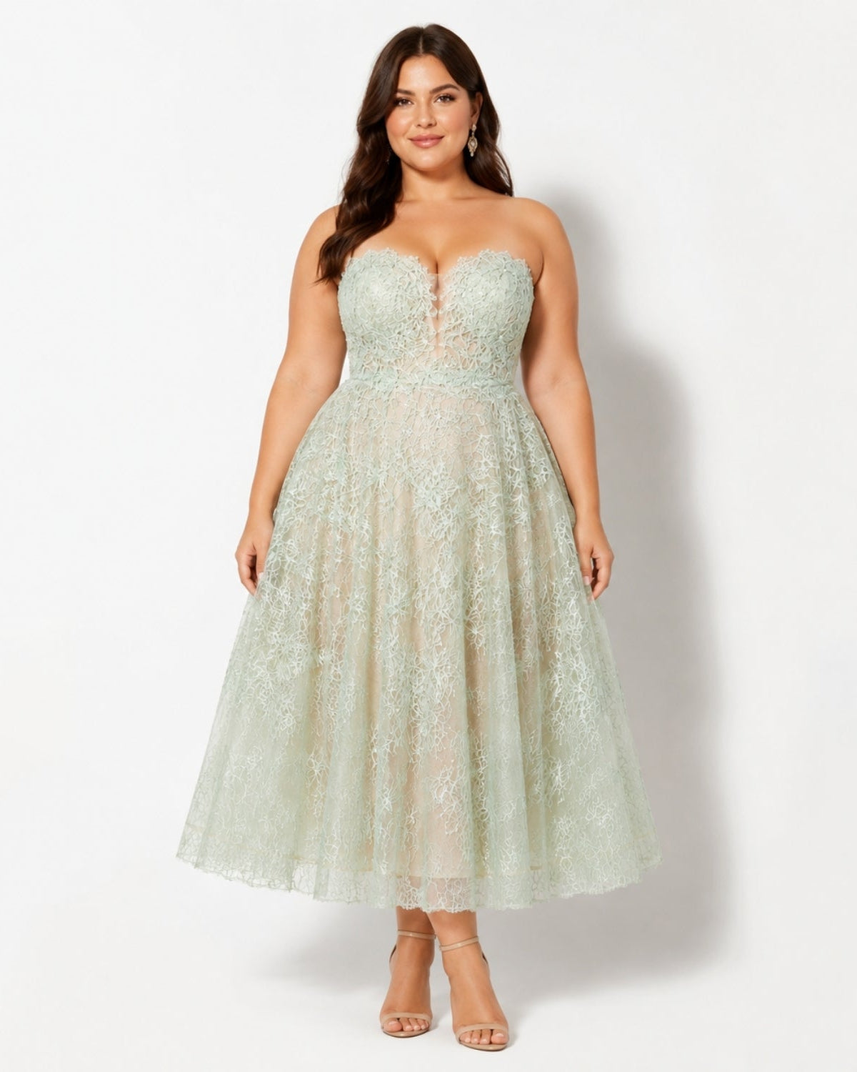 A woman modeling a strapless light sage green lace and tulle midi dress with a sweetheart neckline and a full skirt, standing against a plain white studio background.
