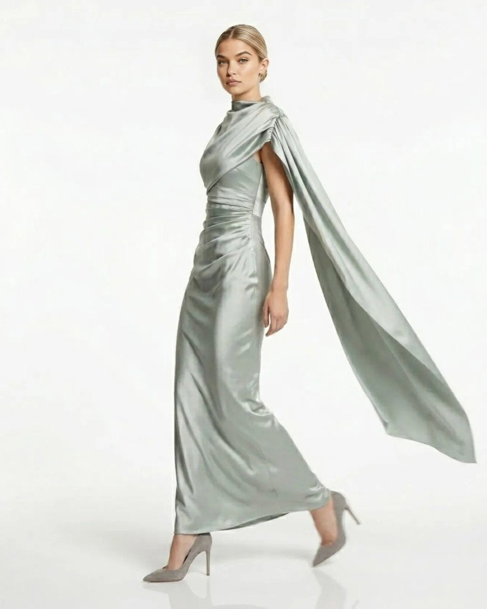Side profile of model walking in the sage green satin formal evening gown with flowing single-shoulder cape detail.