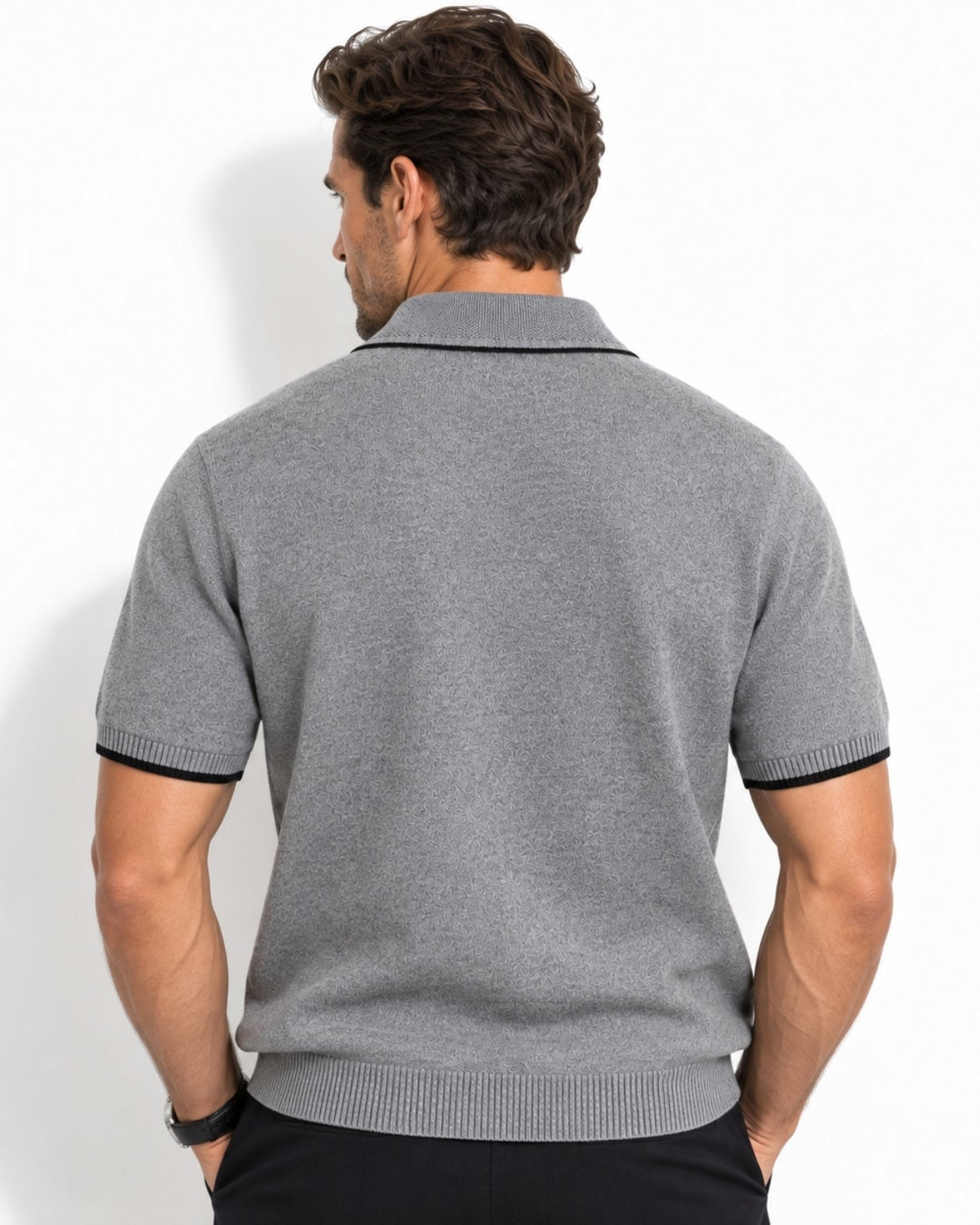 A man viewed from the back wearing a gray short-sleeve knit polo shirt with black trim on the collar and sleeve cuffs, paired with black pants, against a plain white studio background.