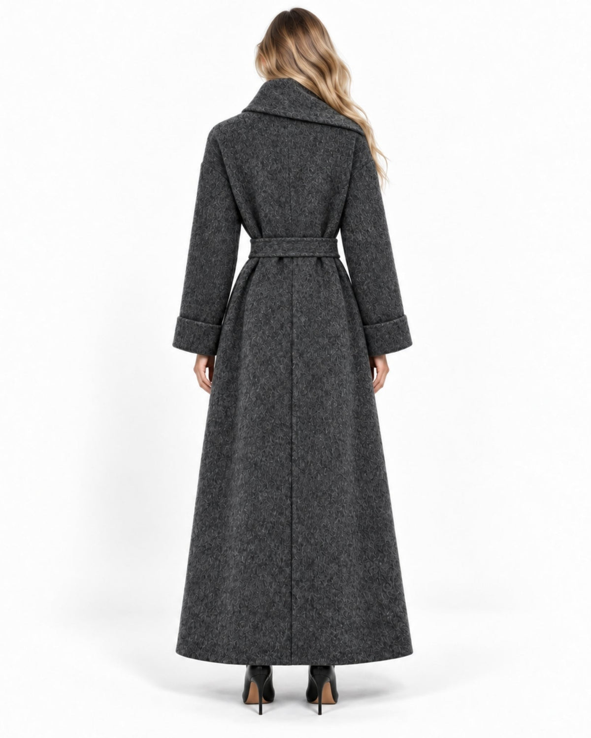 A woman viewed from the back wearing a long dark gray belted coat with a wide collar and long sleeves, paired with black heels, against a plain white studio background.