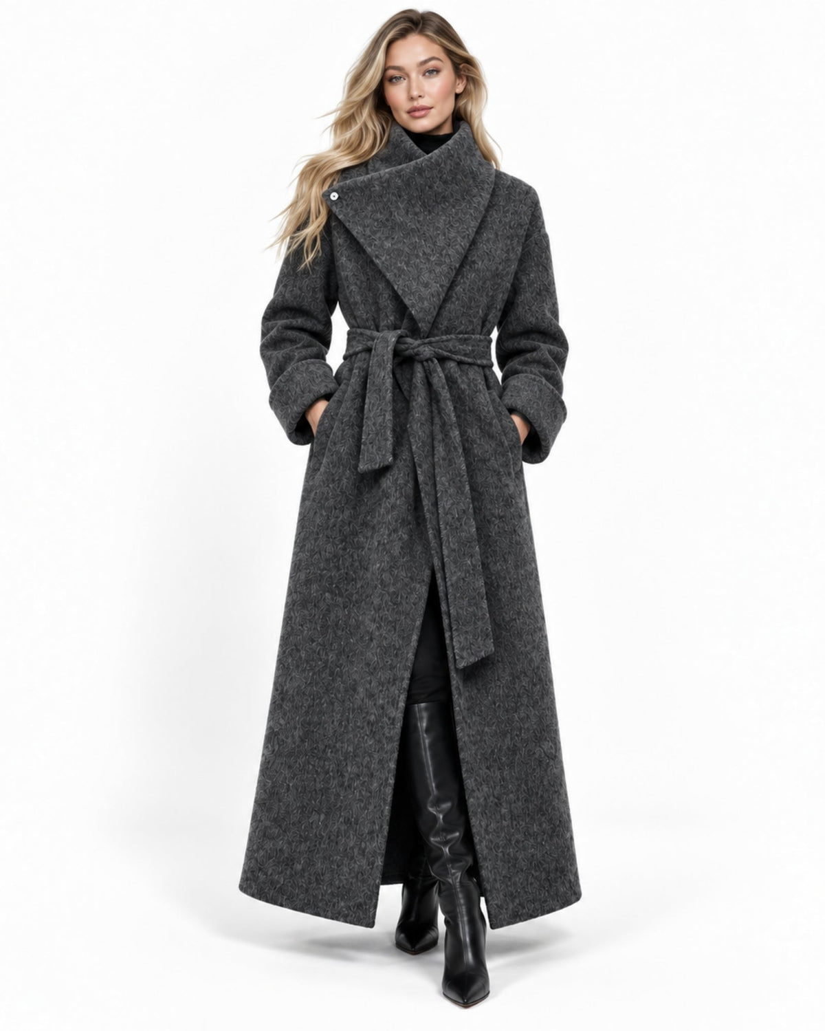 A woman modeling a long charcoal gray wrap coat with a wide shawl collar, tie belt, and front slit, paired with black knee-high boots against a plain white studio background.