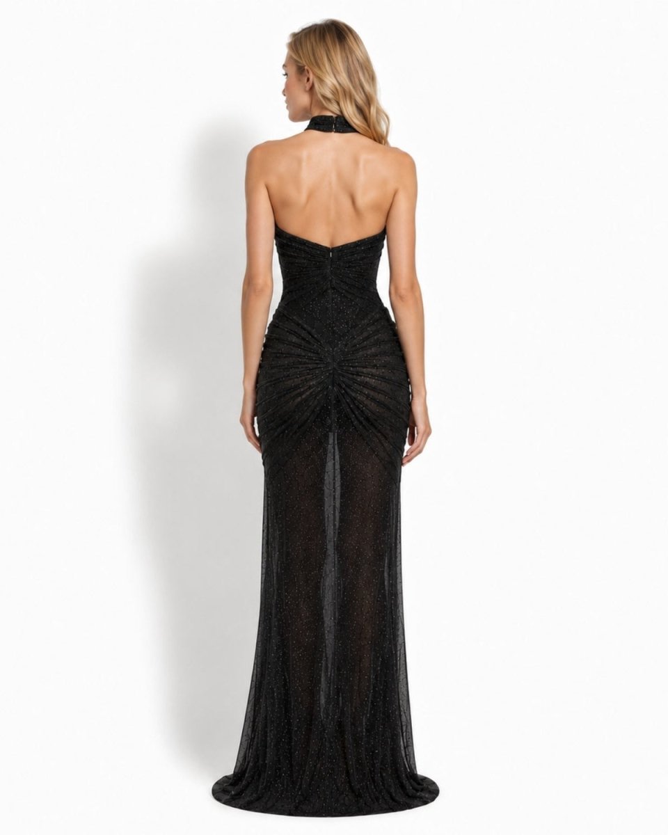 A woman modeling a strapless black evening gown from the back, featuring a structured corset-style bodice, ruched back, and sheer textured skirt, set against a plain white studio background.