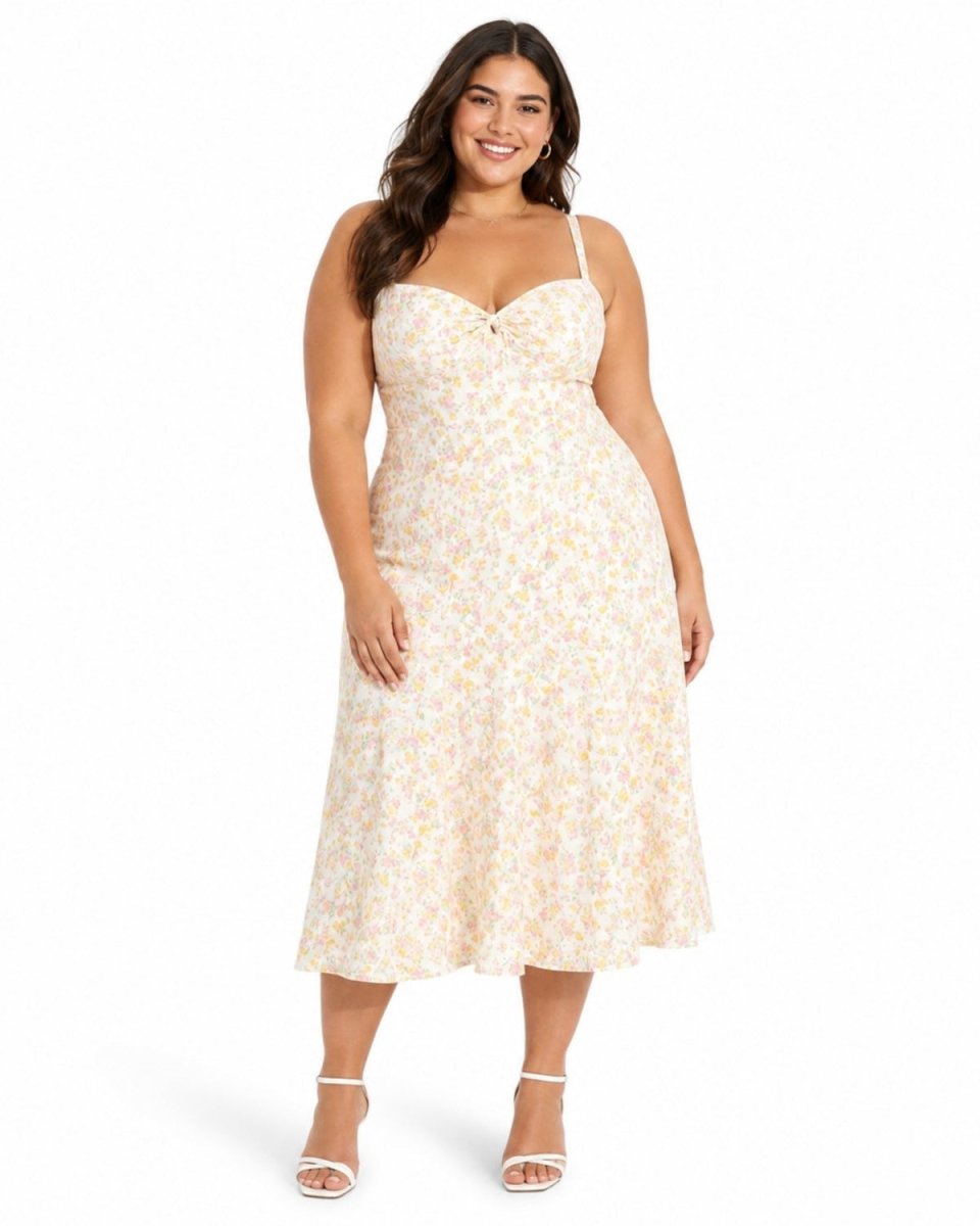 A woman modeling a sleeveless midi dress with a sweetheart neckline, thin straps, and a delicate yellow and white floral print on a cream background, paired with white heeled sandals against a plain white studio background.