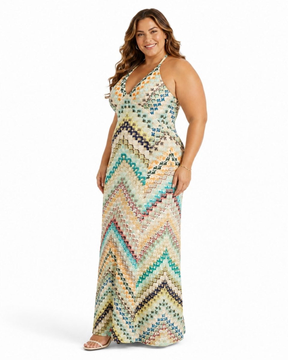 A woman modeling a sleeveless, floor-length maxi dress with a colorful zigzag chevron pattern in beige, teal, brown, and black on a plain white studio background.