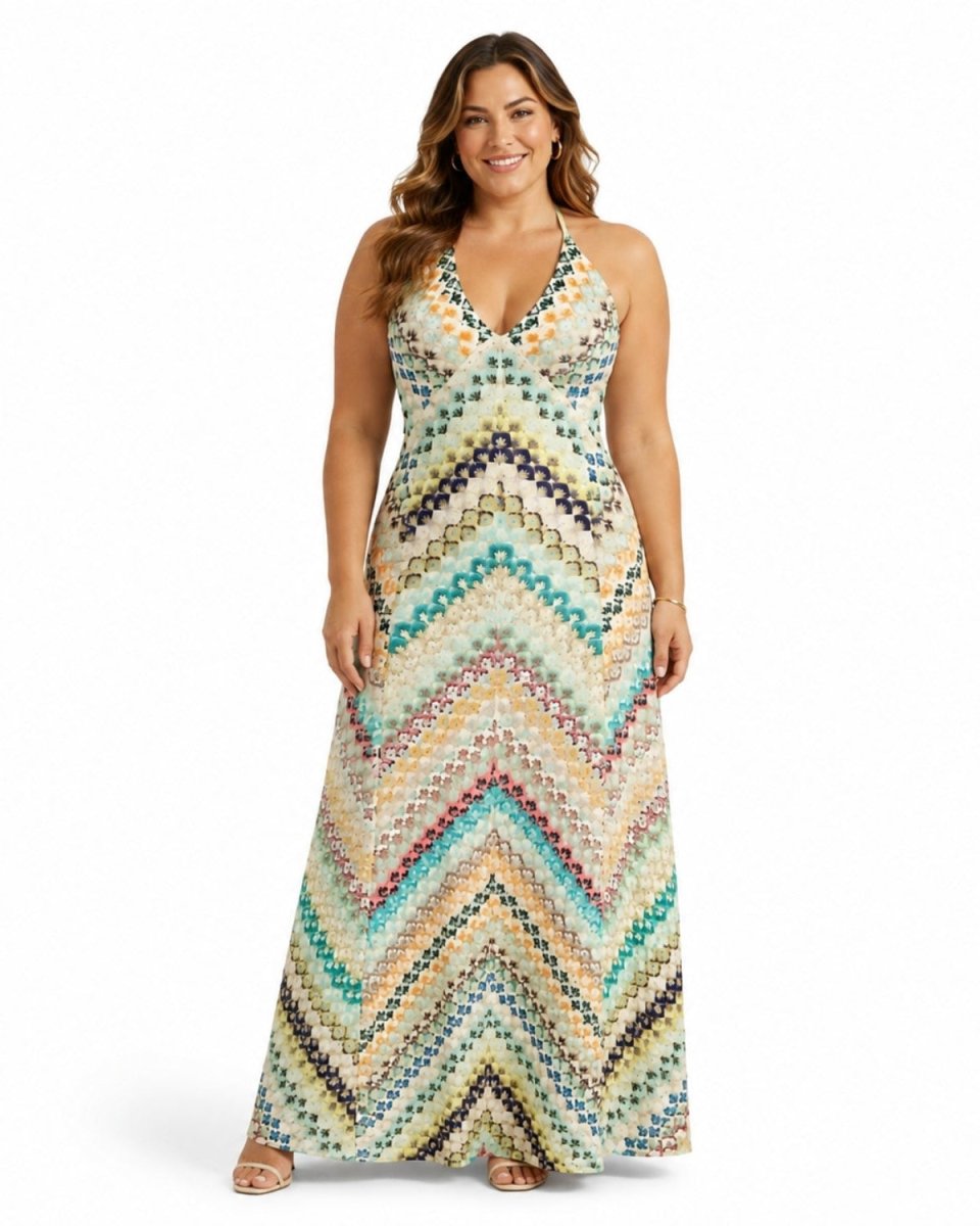 A woman modeling a sleeveless halter-neck maxi dress with a colorful chevron pattern in shades of teal, beige, brown, and blue, set against a plain white studio background.