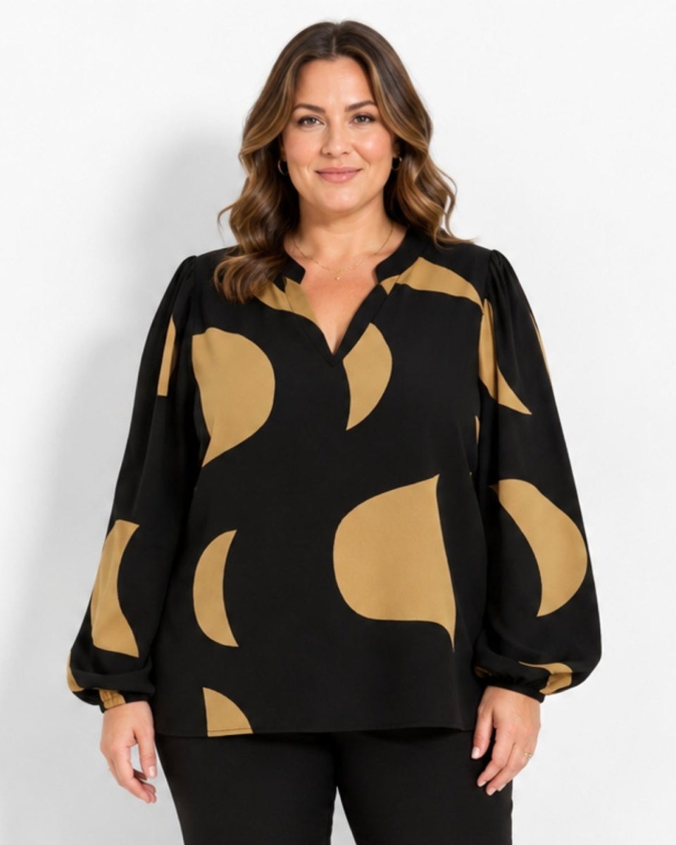A woman modeling a black long-sleeve blouse with a tan abstract organic pattern, set against a plain light gray studio background.