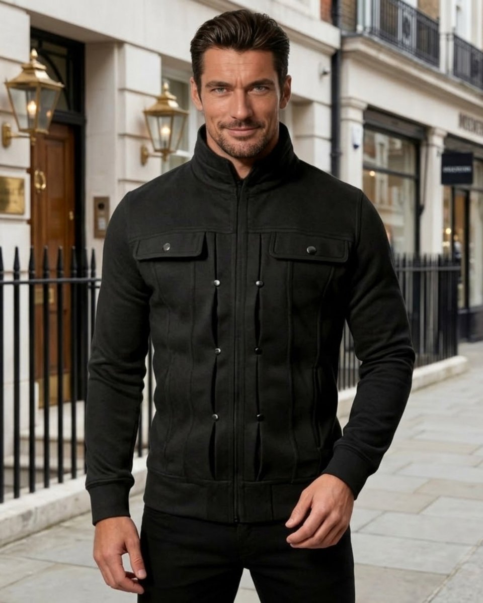 A man wearing a black zip-up jacket with a stand-up collar and flap chest pockets, standing on a city sidewalk in front of a building.