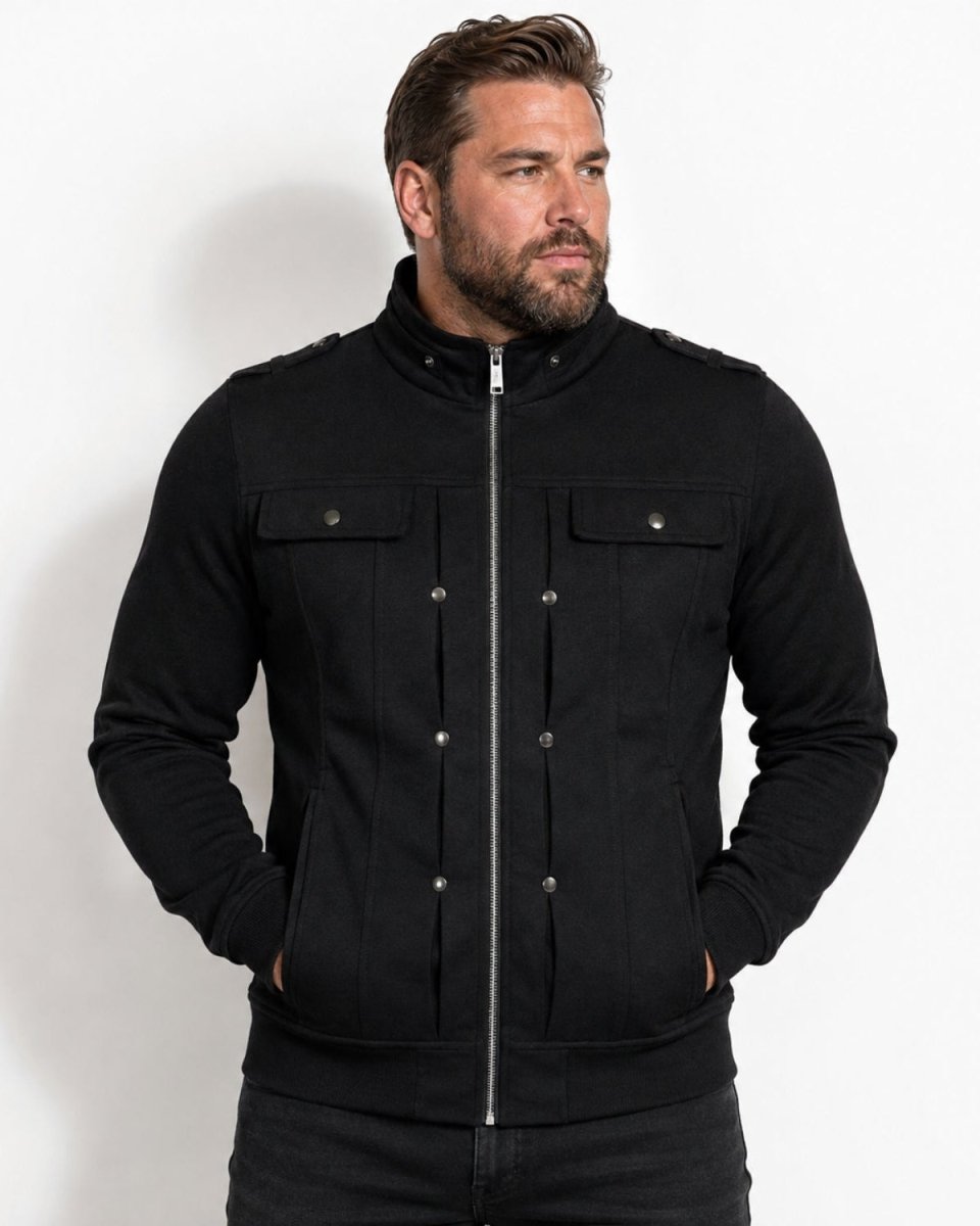 A man wearing a black zip-up jacket with snap-button details on the chest, photographed against a plain white studio background.