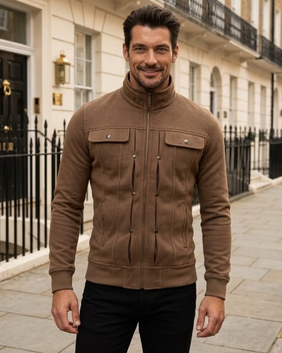 A man wearing a brown zip-up jacket with a stand-up collar and chest flap pockets, standing on a city sidewalk in front of classic stone buildings.