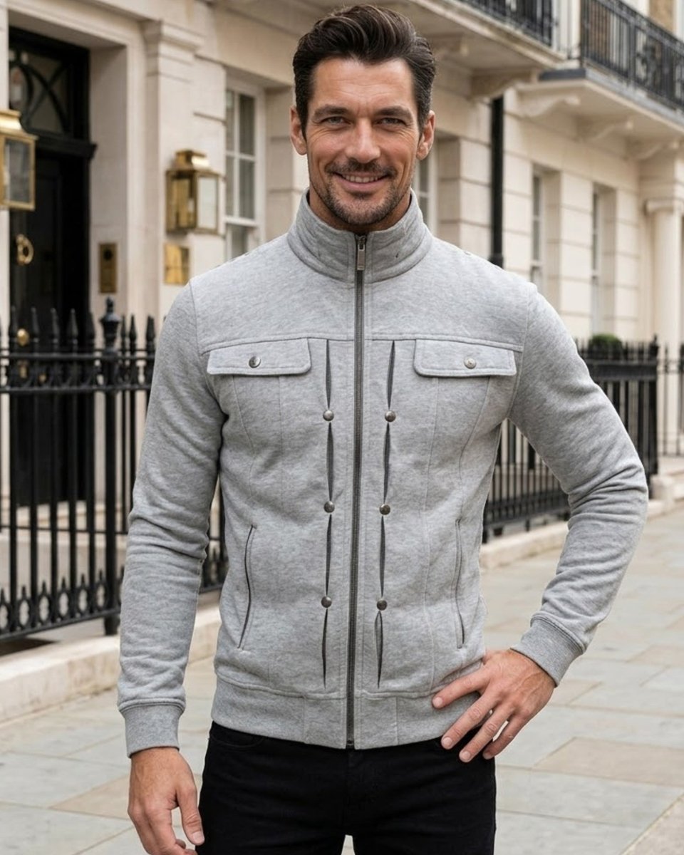A man wearing a light gray zip-up jacket with a mock neck and snap-button details, standing on a city street in front of a classic building.