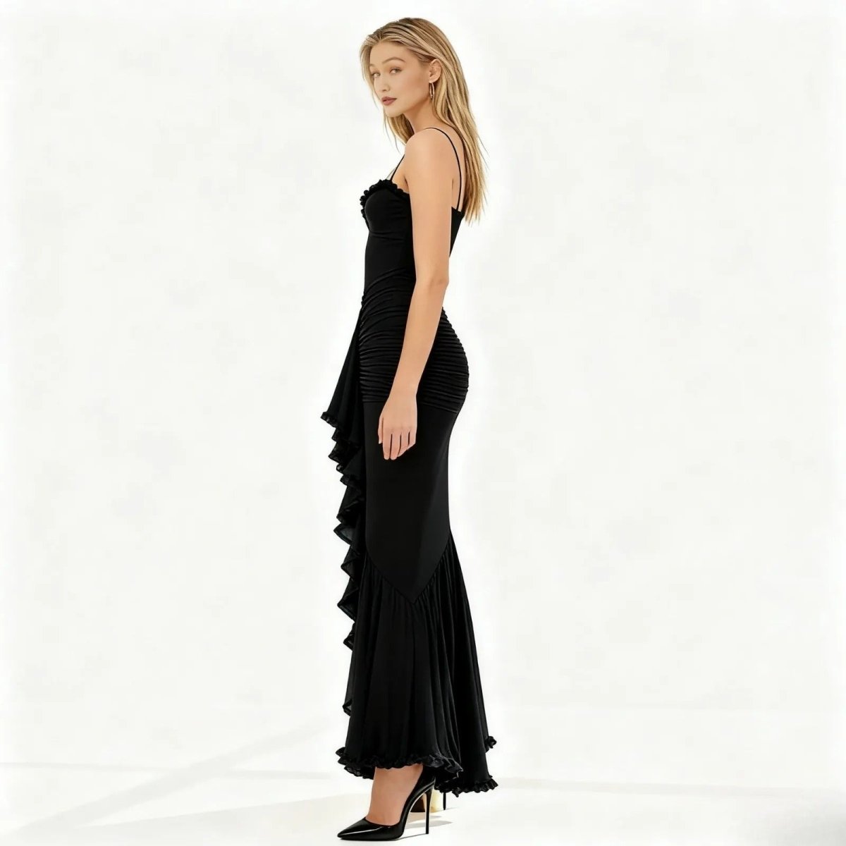 A female model wearing the Kouvr Fashion long black mermaid gown with a sweetheart neckline and a damalia ruffle down the side, on a white background.