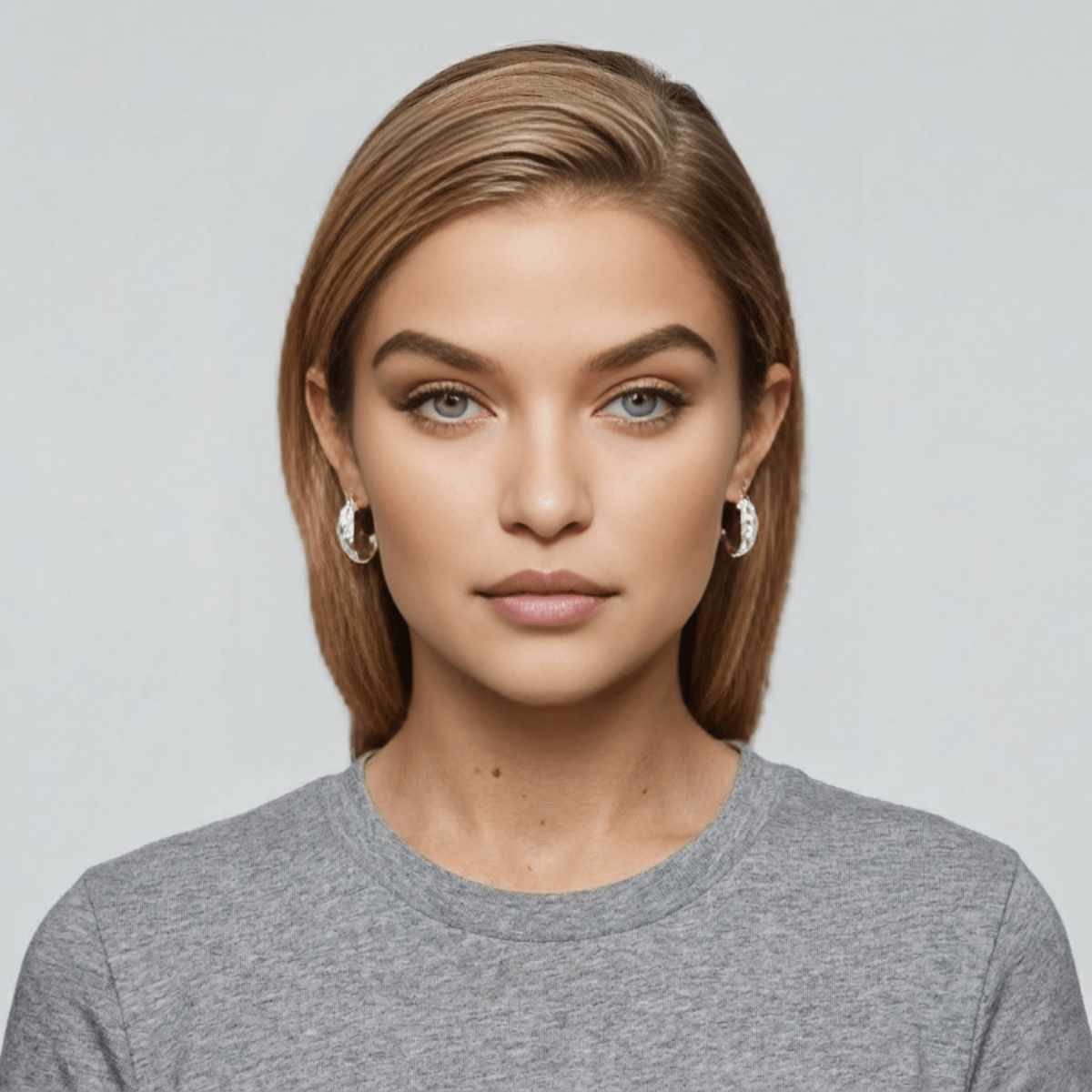 A woman with blonde hair and blue eyes wearing a pair of sparkling, wide pavé diamond hoop earrings, shown in a silver-tone metal to demonstrate scale.