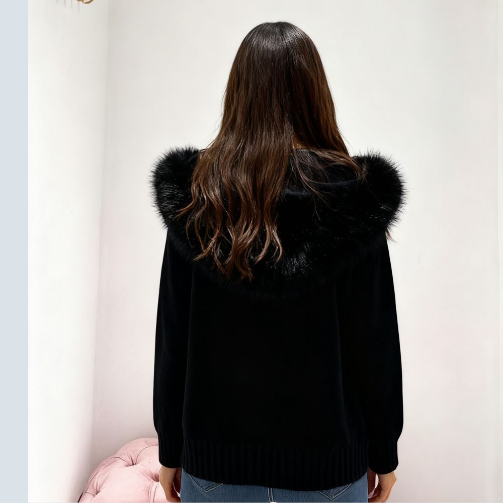 Person wearing a black kouvr coat with fur trim, standing against a plain background