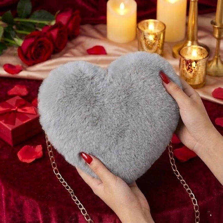 A woman wearing a black heart-print dress with a grey faux fur heart-shaped bag with a gold chain strap resting on her lap at a cafe table.