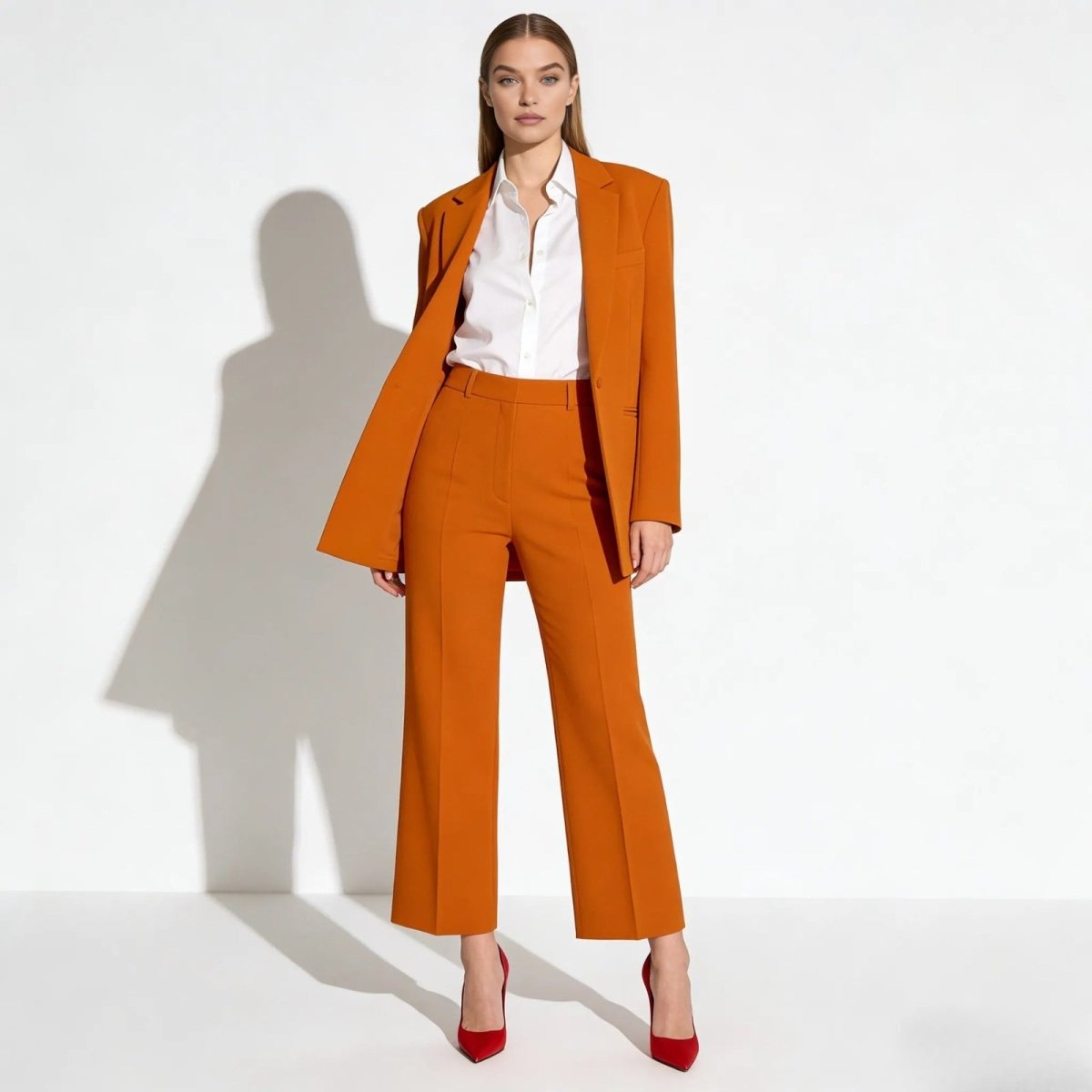 Model wearing the Kouvr Fashion kate orange pantsuit featuring a relaxed-fit blazer and high-waisted wide-leg trousers, styled with a white shirt and red heels.