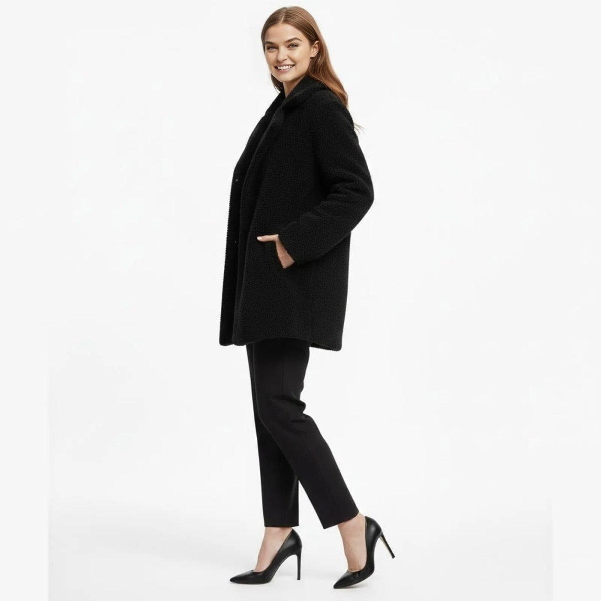 Side view of a woman smiling while wearing the Kouvr Fashion black sherpa winter coat, showing its mid-length and fit.