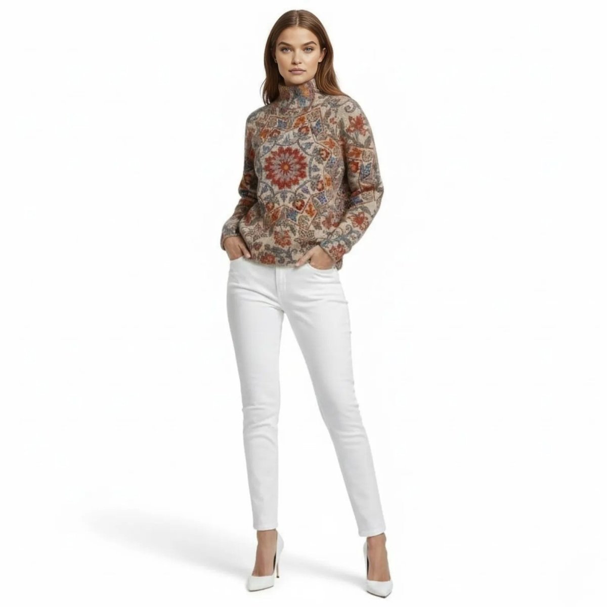 Model wearing the Kouvr Fashion artisanal Regina turtleneck sweater with a central mandala pattern in orange and blue, styled with white jeans.