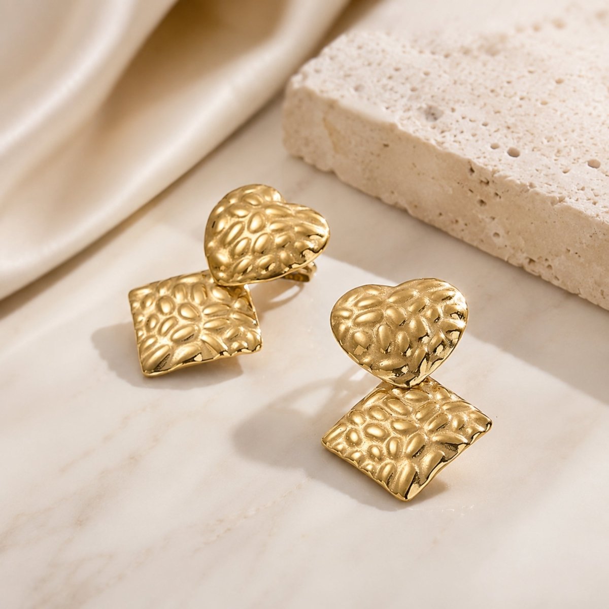 Close up detail of Kouvr gold hammered heart and geometric rhombus earrings showing light reflecting texture