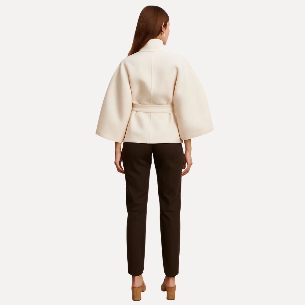 Model wearing the Kouvr Jannah Wool Cape Jacket in White, featuring a high funnel neck and tie-waist belt." For the back view