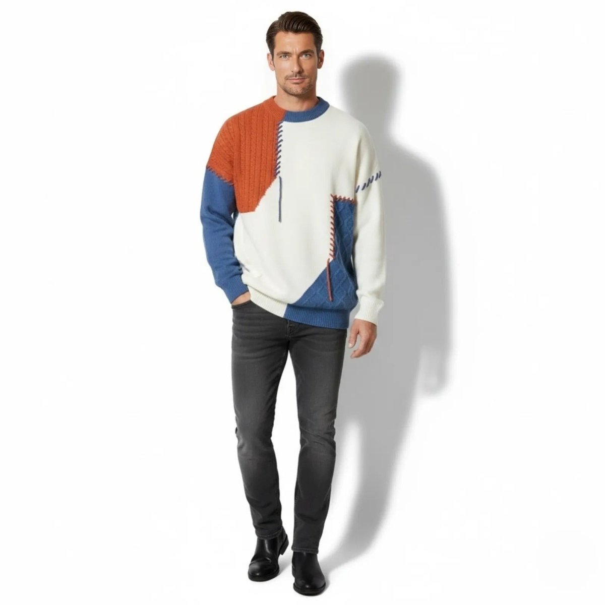 Male model wearing the Kouvr Miller Patchwork Sweater in white, orange, and white, looking at the camera with his hand in his dark jeans pocket.
