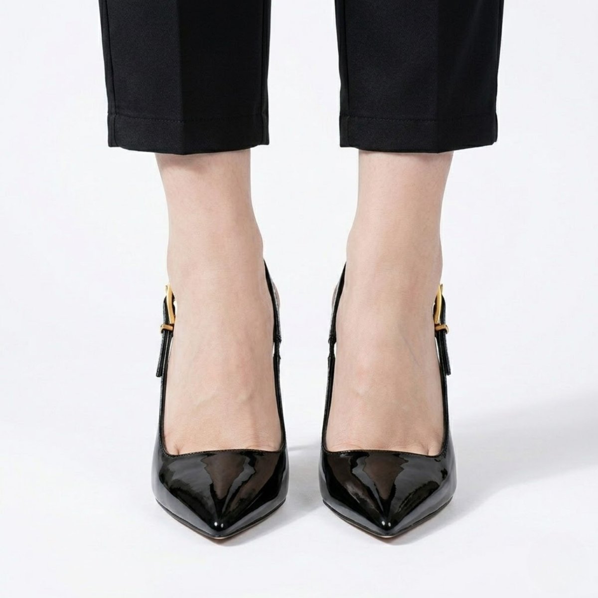 Front view of a model's feet wearing black pointed-toe patent leather slingback pumps from Kouvr.