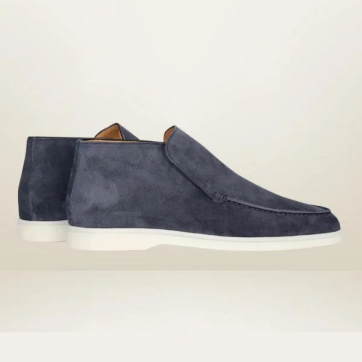Kouvr suede ankle loafer boots with tan chino pants.
Side view of black Italian suede slip-on boots with a contrasting white sole, worn by a model.