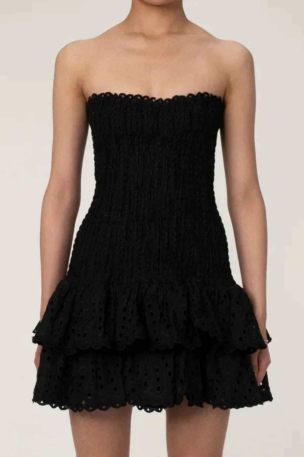 Model wearing Kouvr Starla black strapless smocked mini dress with tiered eyelet skirt