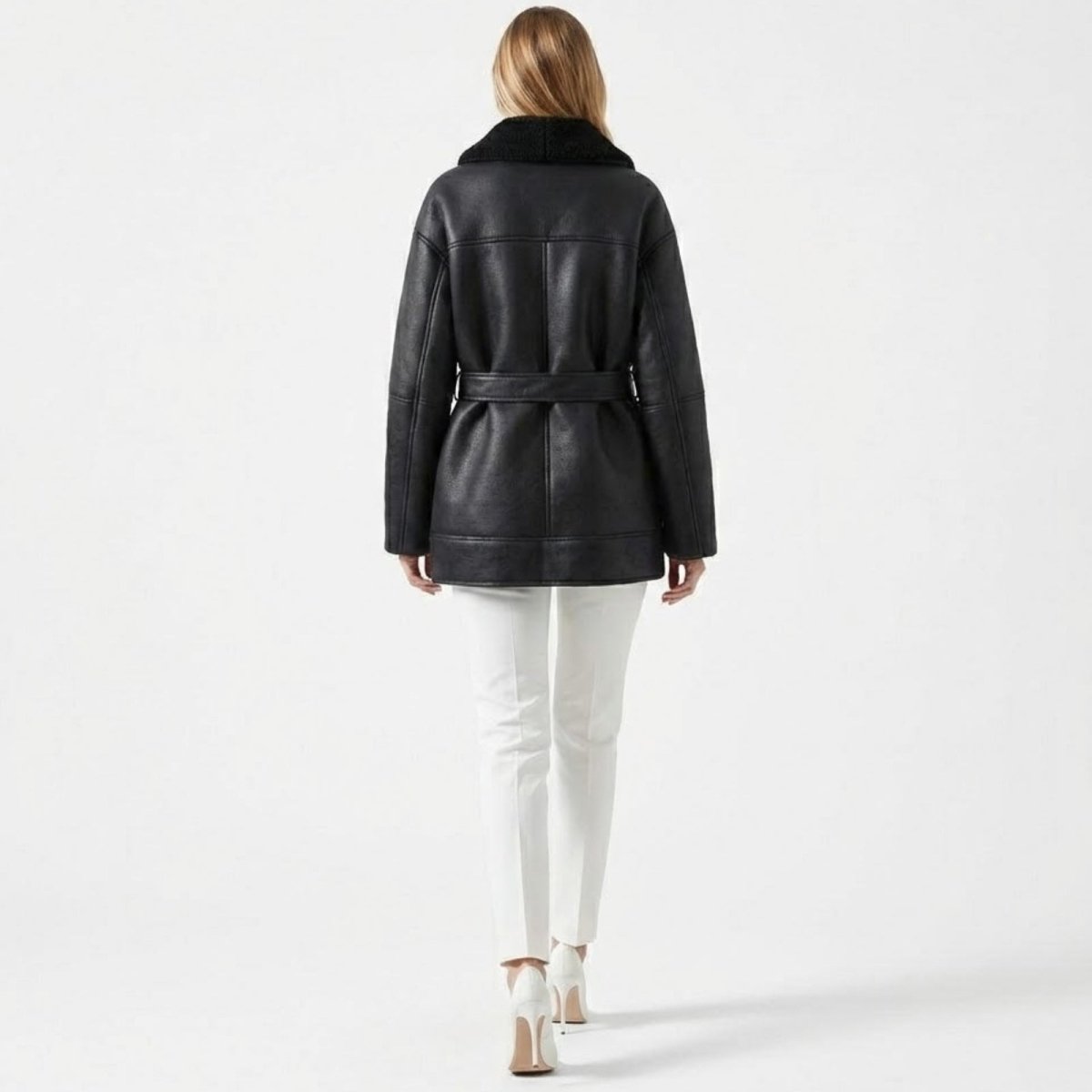 Back view of a female model wearing the Suzanne black belted shearling jacket by Kouvr, showcasing the seam details and fit.