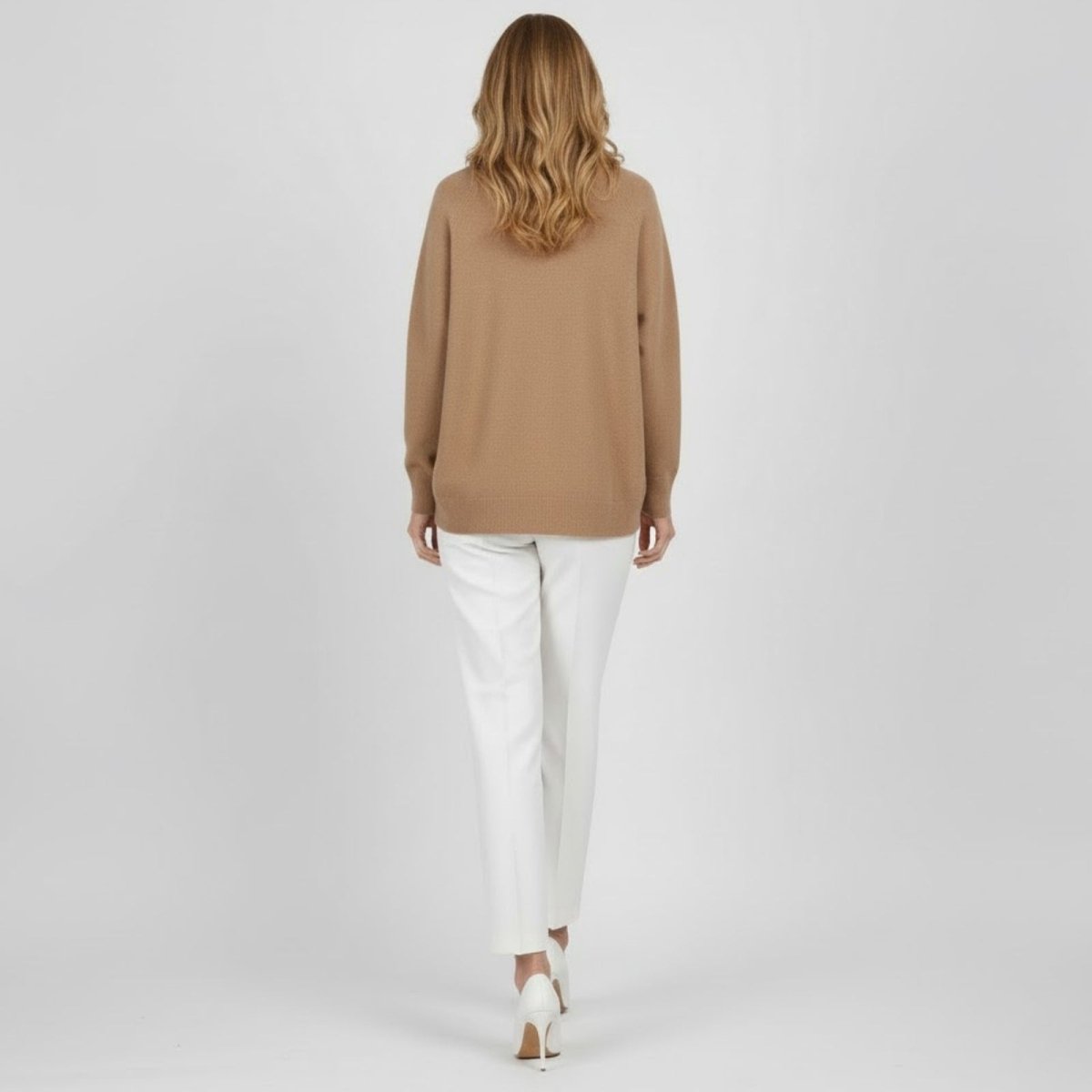 Back view of a model walking away wearing a light brown oversized knit sweater, showcasing its drape.