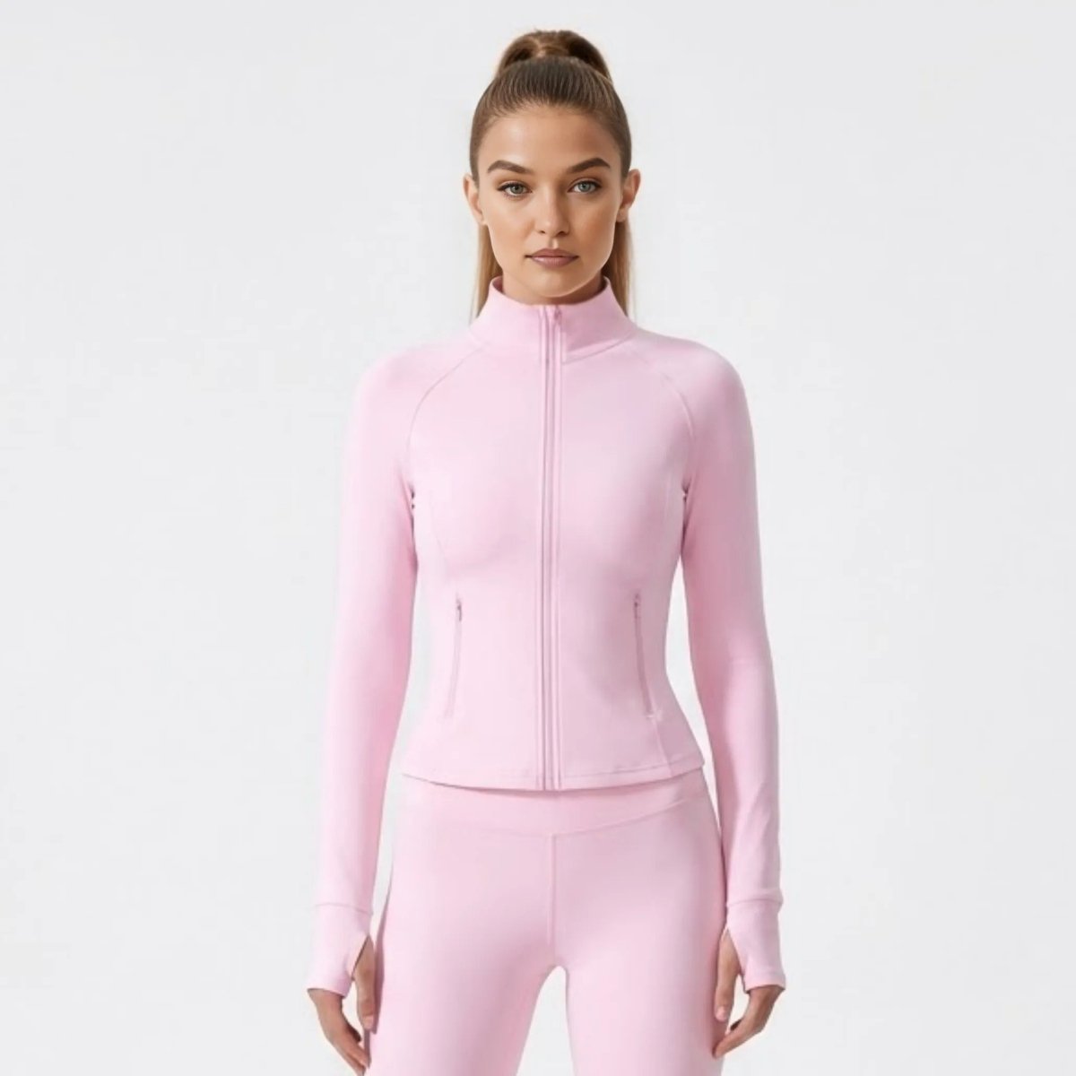 Front view of female model wearing Kouvr premium light pink fitted zip-up activewear jacket with mock neck and thumbholes.