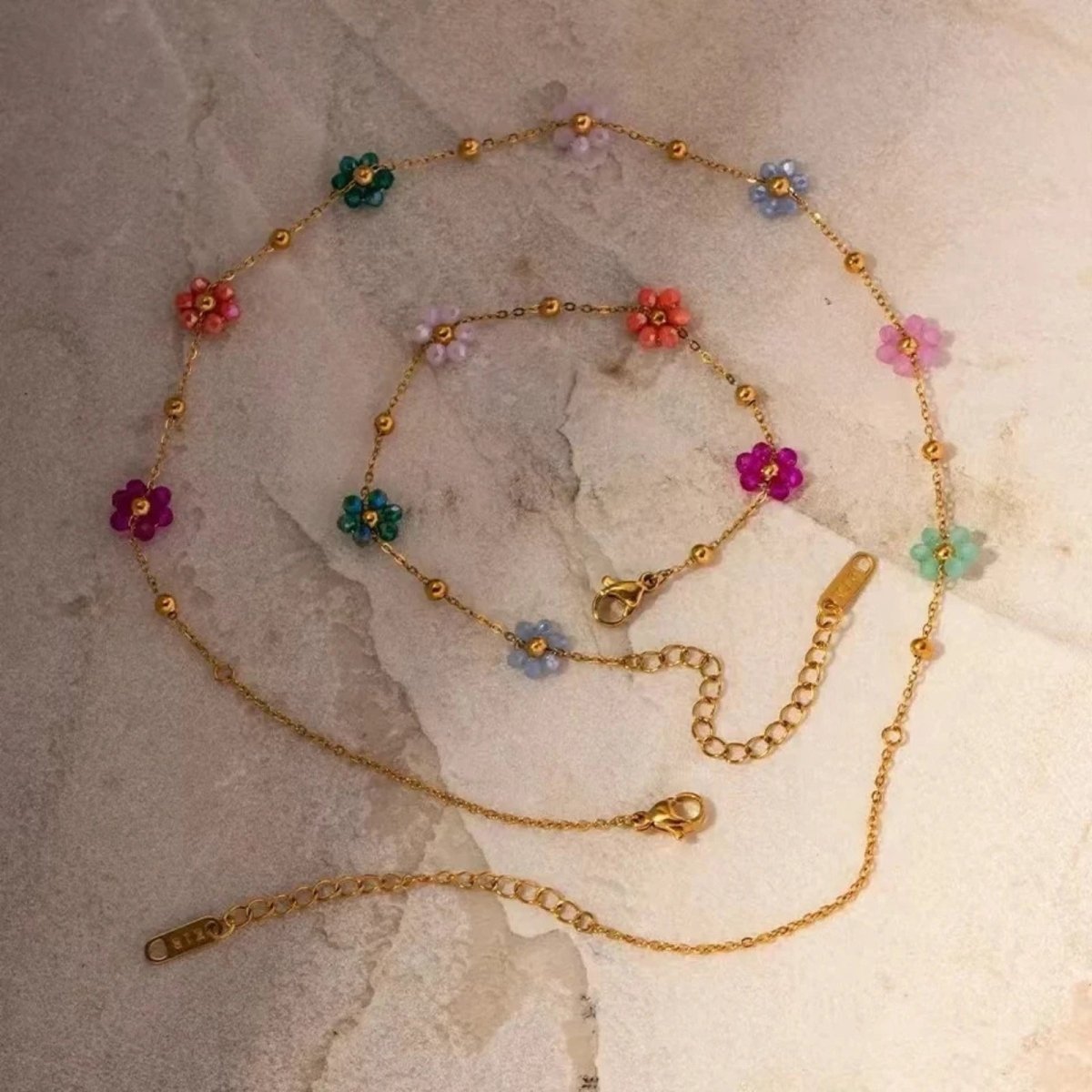 Flatlay product shot of the Kouvr Ysabel set beaded flower necklace and bracelet set arranged artfully on a textured light marble surface.