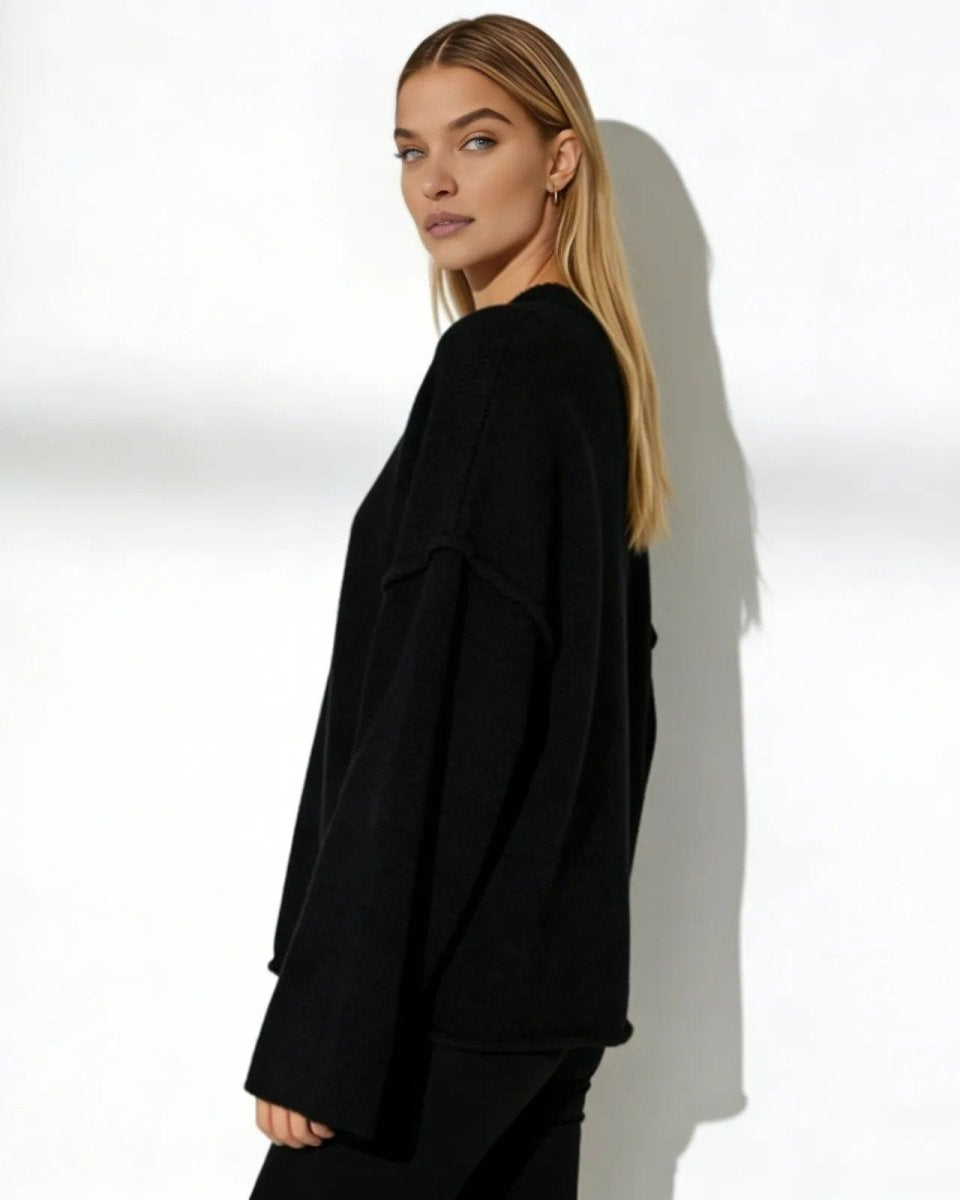 Side profile of a woman in an oversized black wool and cashmere blend sweater, highlighting the dramatic flared sleeve silhouette.