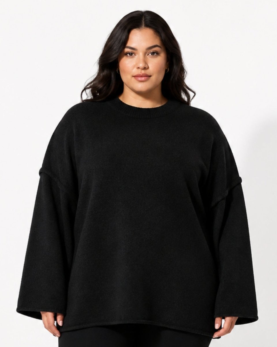 A woman modeling an oversized black crewneck sweater with wide, slightly dropped shoulders, photographed against a clean white studio background.
