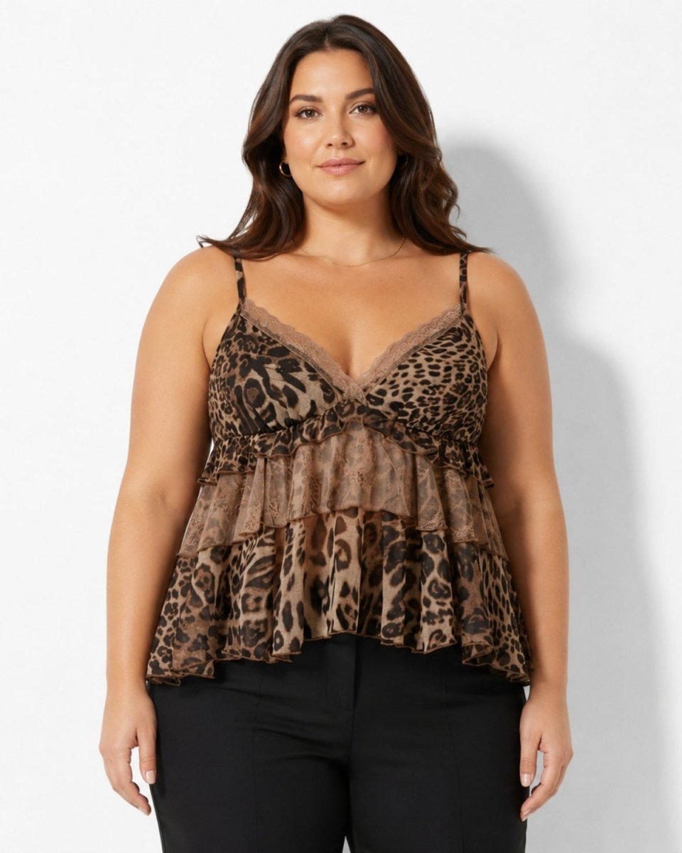 A woman modeling a leopard print camisole top with thin straps and a ruffled peplum hem, paired with black pants, against a light gray studio background.